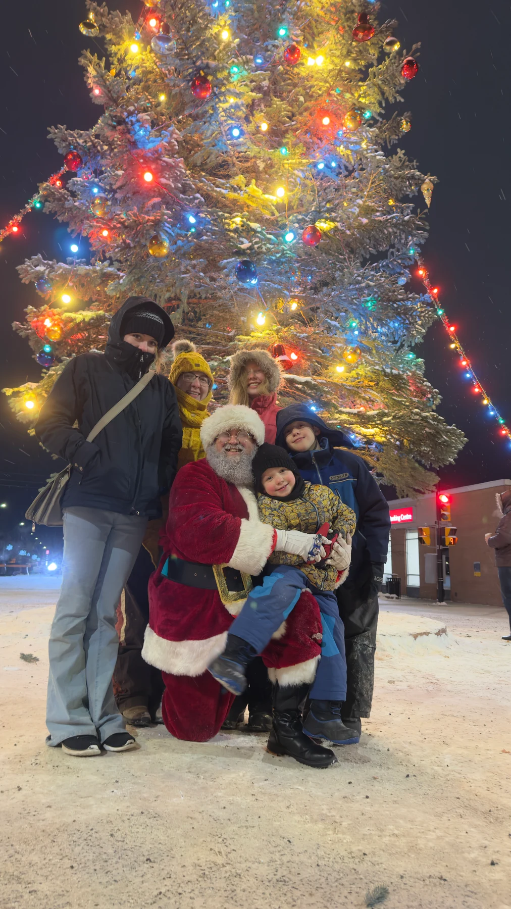 Santa Bryce and his family beside a snow-covered town Christmas tree